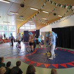 Schüler und Schülerinnen mit blauen Rockerperücken fahren auf Einrädern durch die Manege. (vergrößerte Bildansicht wird geöffnet)