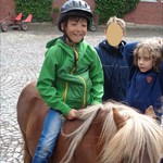 Jamie ist auf einem Pony geritten. Das Pony hat die Mähne im Gesicht. Ich bin auf dem gleichem Pony geritten und das Pony ist aus Versehen auf Frau Neumanns Fuß getreten. (vergrößerte Bildansicht wird geöffnet)